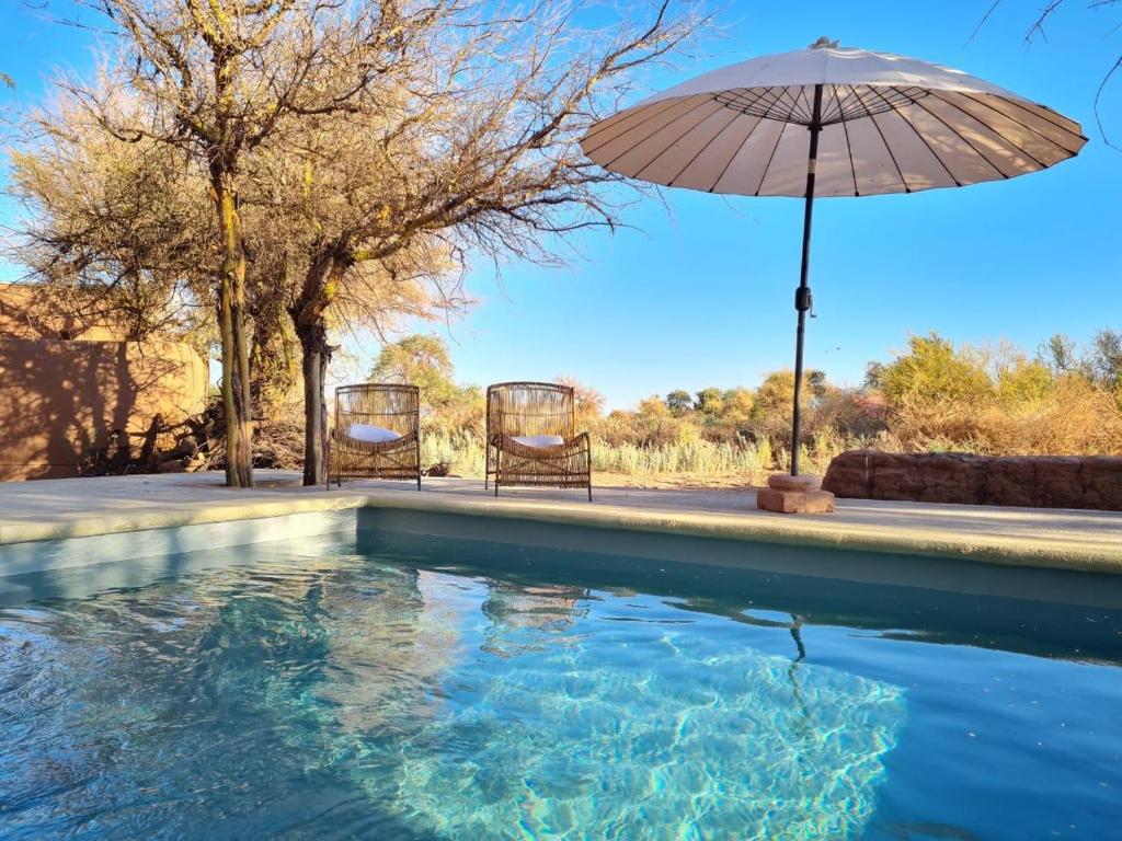 uma piscina com um guarda-sol e duas cadeiras em La Casa de Pascual Andino em San Pedro de Atacama
