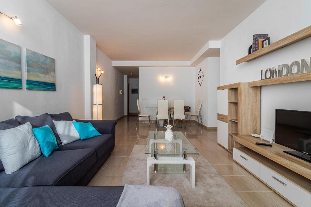 ein Wohnzimmer mit einem blauen Sofa und einem TV in der Unterkunft Flatguest Trebolina - 3Bdr - FastWiFi - Parking in Vecindario
