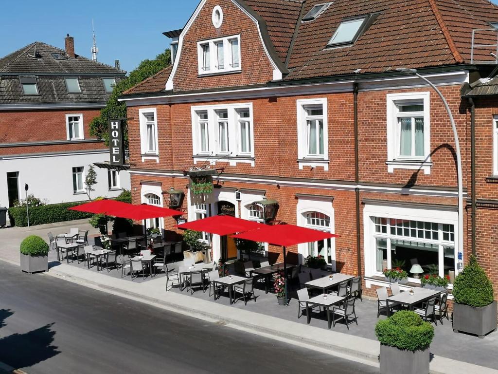 a restaurant with tables and red umbrellas in front of a building at Hotel Lindenhof in Emsdetten