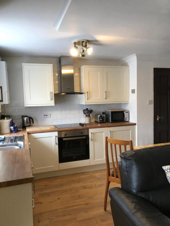 a kitchen with white cabinets and a table and a couch at Black Bull Barn in Kirkby Stephen