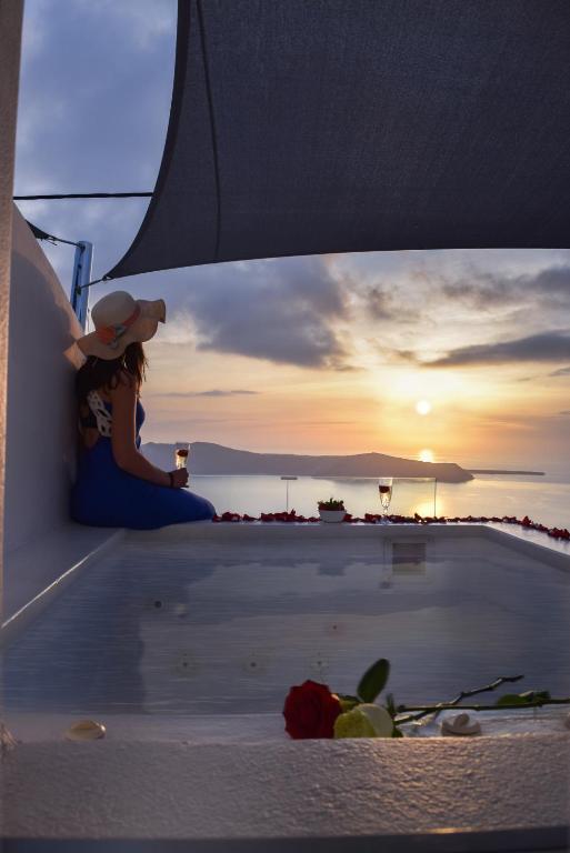 a woman sitting on a boat looking at the sunset at Vitsentzos Suites in Imerovigli