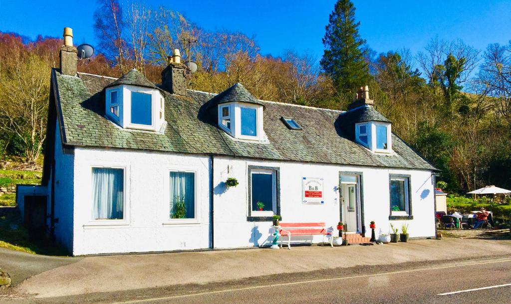 a small white house with blue windows on a street at Rowantreebank Bed and Breakfast in Arrochar