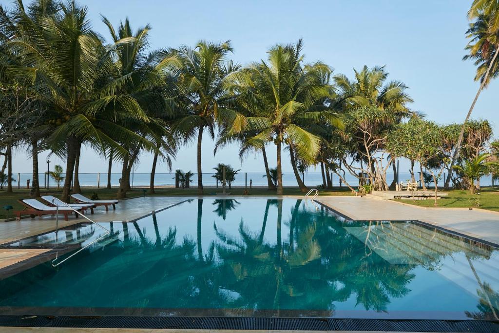a swimming pool with palm trees and the ocean at The Beach Villas by Ceylon Bungalows in Wadduwa