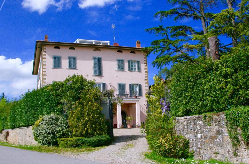 ein großes weißes Haus mit einer Wand und Bäumen in der Unterkunft Villa La Grotta in San Giustino Valdarno