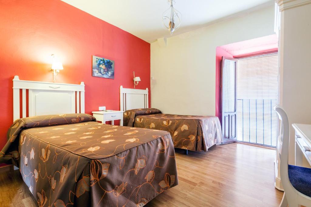 Habitación con 2 camas y paredes rojas. en Hostal El Caballo Blanco, en Osuna