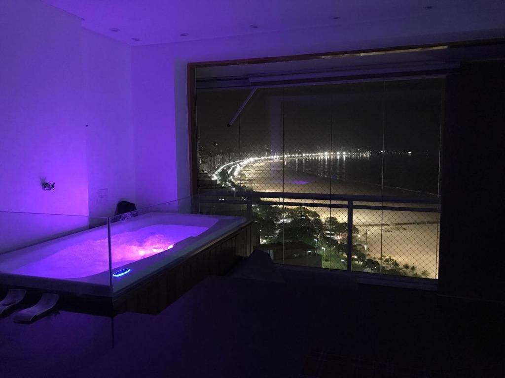 Dieses lila Zimmer verfügt über ein großes Fenster mit einer Badewanne. in der Unterkunft Maravilhoso Apto Vista Mar Jacuzzi Wi Fi Pé Areia in Santos