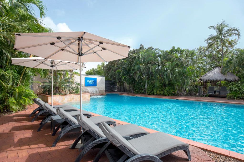 a group of chairs and an umbrella next to a swimming pool at Mantra Frangipani Broome in Broome