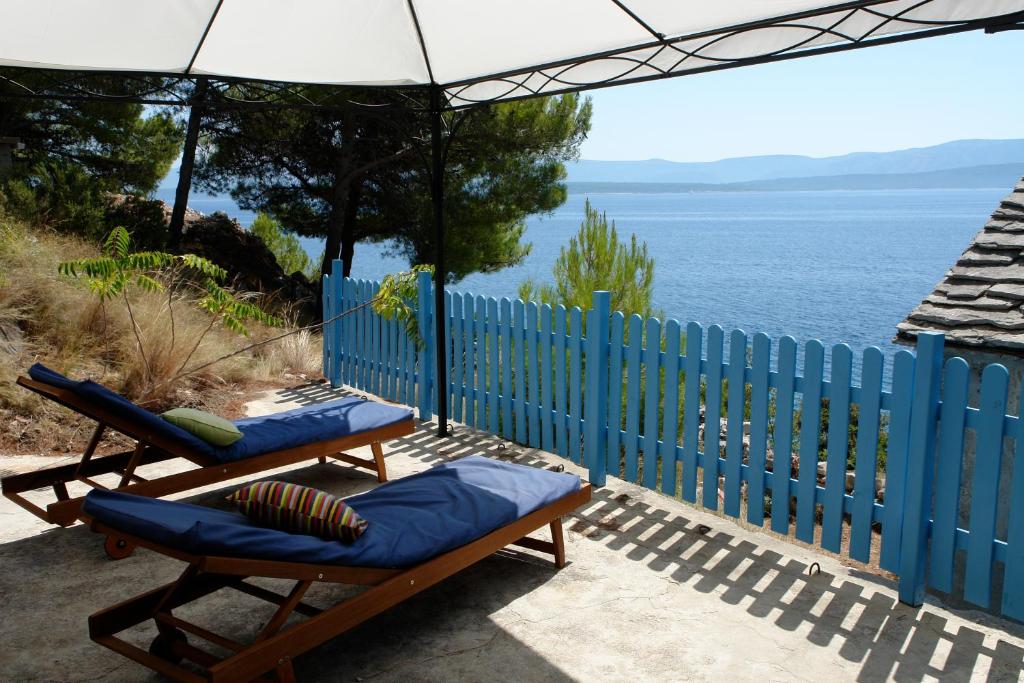 a patio with two chairs and an umbrella and the ocean at A small stone house by the sea, in a wineyard in Nerežišća