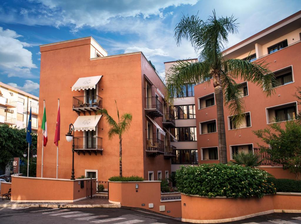 a building with palm trees in front of it at Artemis Hotel in Cefalù