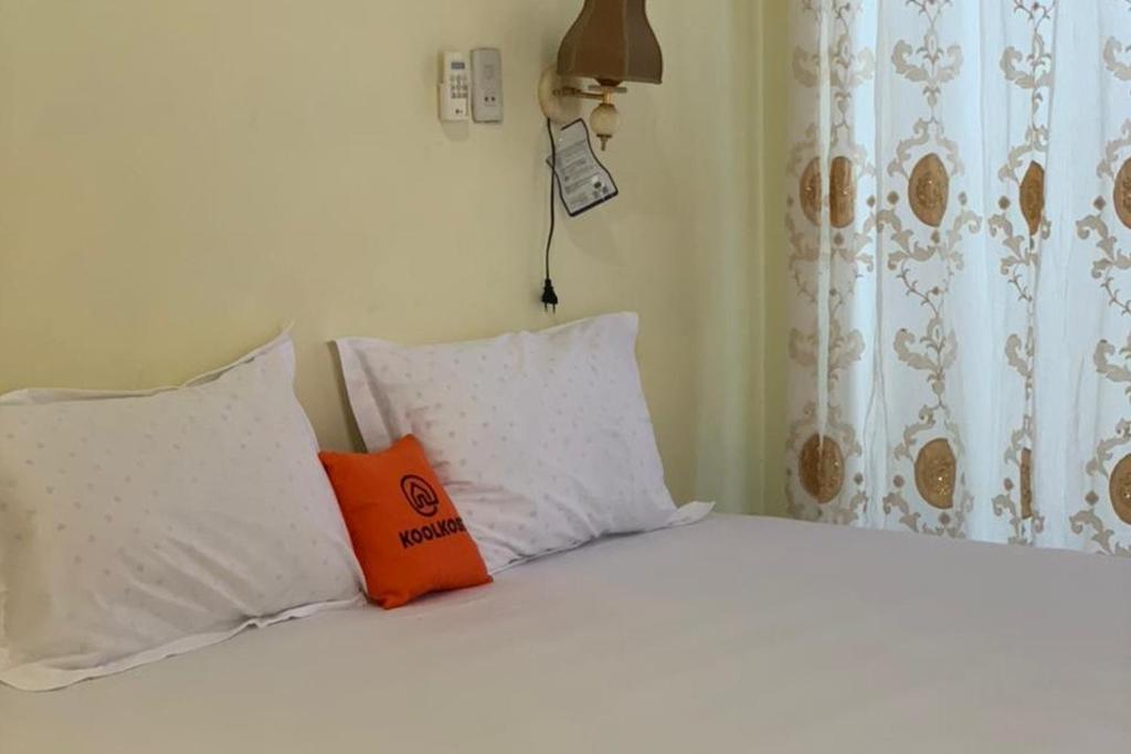 Una cama blanca con una almohada naranja. en KoolKost near Budi Mulia Siantar en Pematangsiantar
