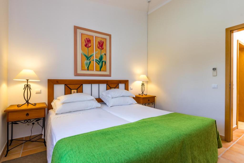 a bedroom with a large white bed with a green blanket at Pestana Palm Gardens in Carvoeiro
