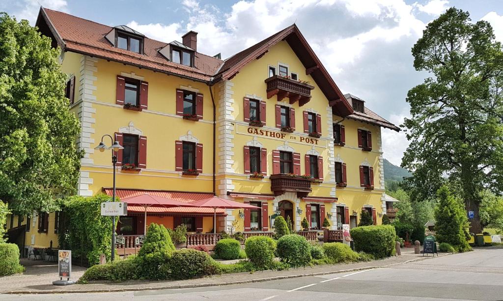 a yellow building with red shutters on a street at Hotel Gasthof Post in Bruck an der Großglocknerstraße