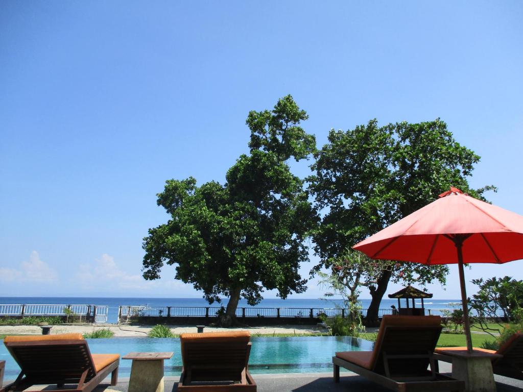 a pool with chairs and an umbrella and the ocean at mascot hotel senggigi in Senggigi