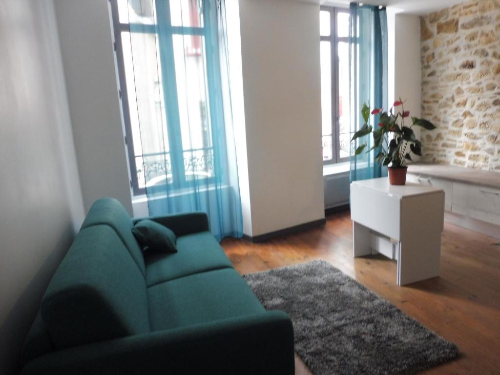 a living room with a green couch and some windows at Studio de charme au centre ville in Salies-de-Béarn