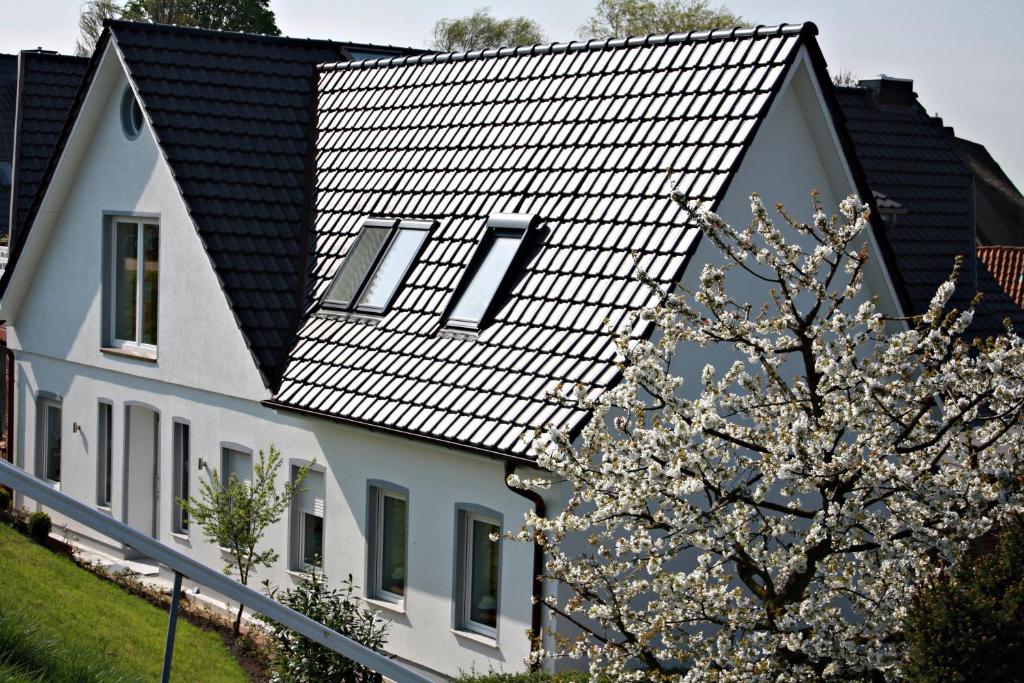 een wit huis met een zwart dak en een bloeiende boom bij Fewo Lüheblick im Haus Lühegarten in Grünendeich