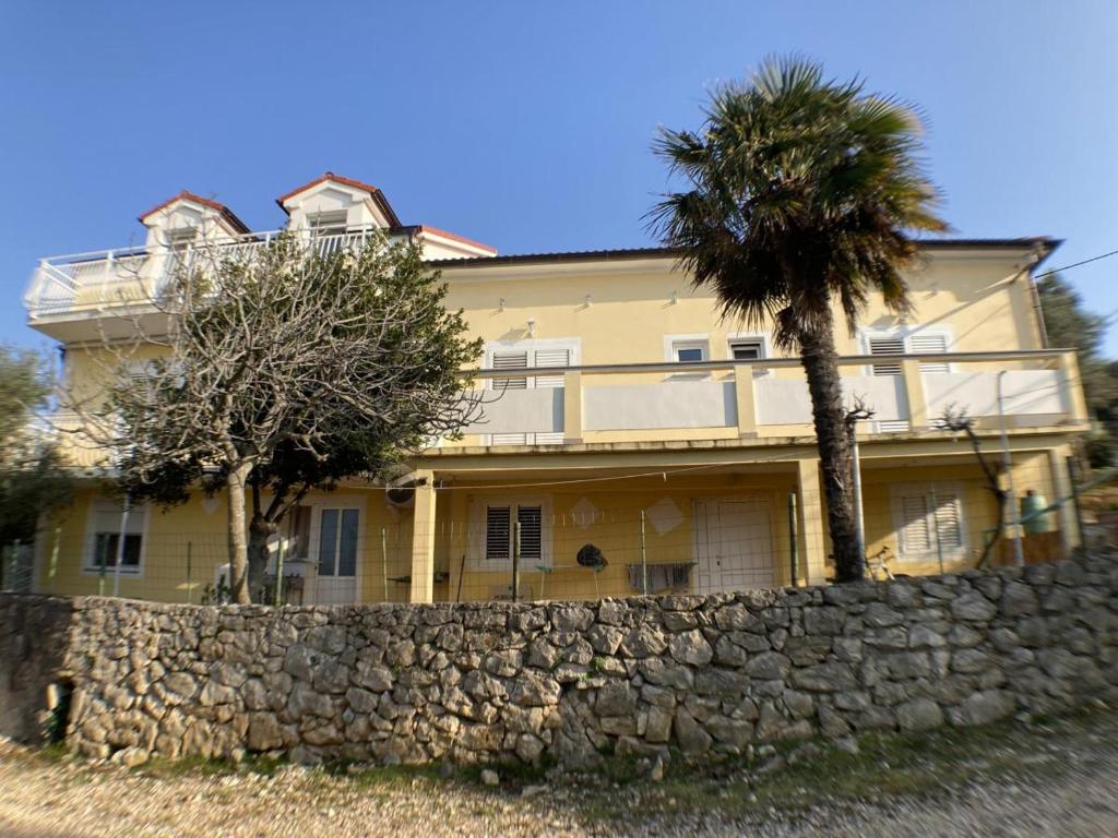 una gran casa amarilla con una pared de piedra y una palmera en Apartmani Marko en Lun