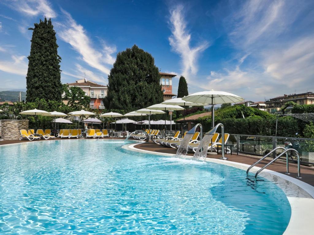 a large swimming pool with chairs and umbrellas at Hotel Villa Mulino ***S in Garda