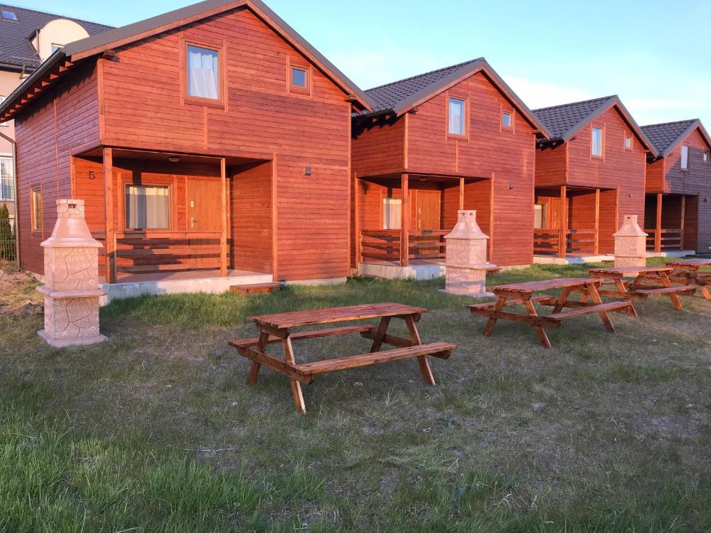 a row of wooden lodges with picnic tables in the grass at Domki Prestige in Ustronie Morskie