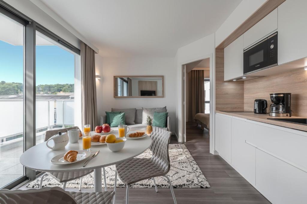 a kitchen and a living room with a table with fruit on it at Lagrange Apart&#39;Hôtel Antibes Olympie in Antibes