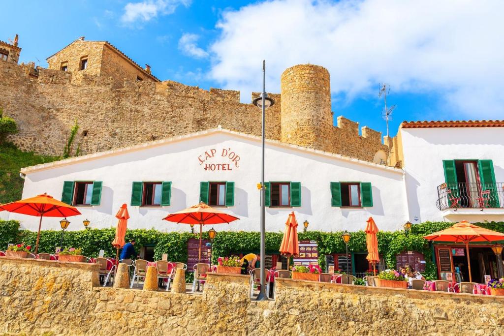 ein Gebäude mit Tischen und Sonnenschirmen davor in der Unterkunft Hotel Cap d'Or in Tossa de Mar