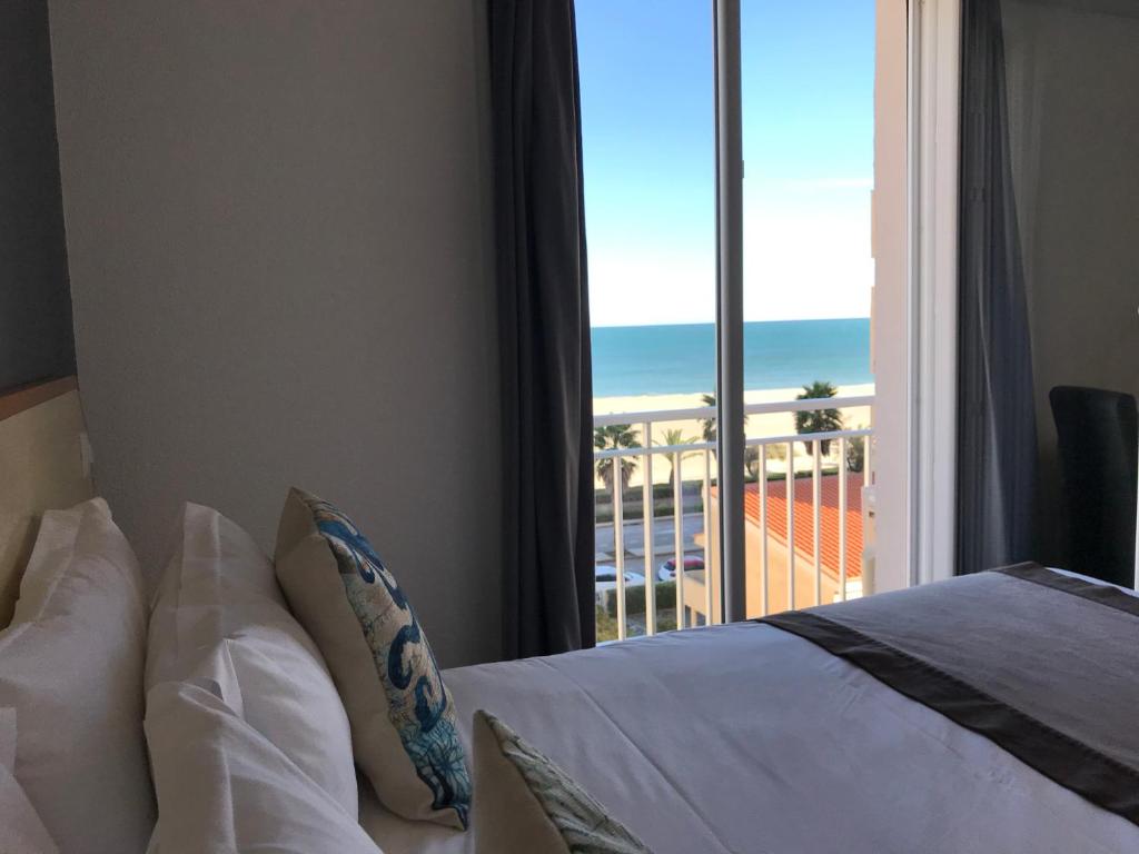 a bedroom with a bed and a view of the ocean at Le Regina Hôtel et restaurant Canet-plage in Canet-en-Roussillon