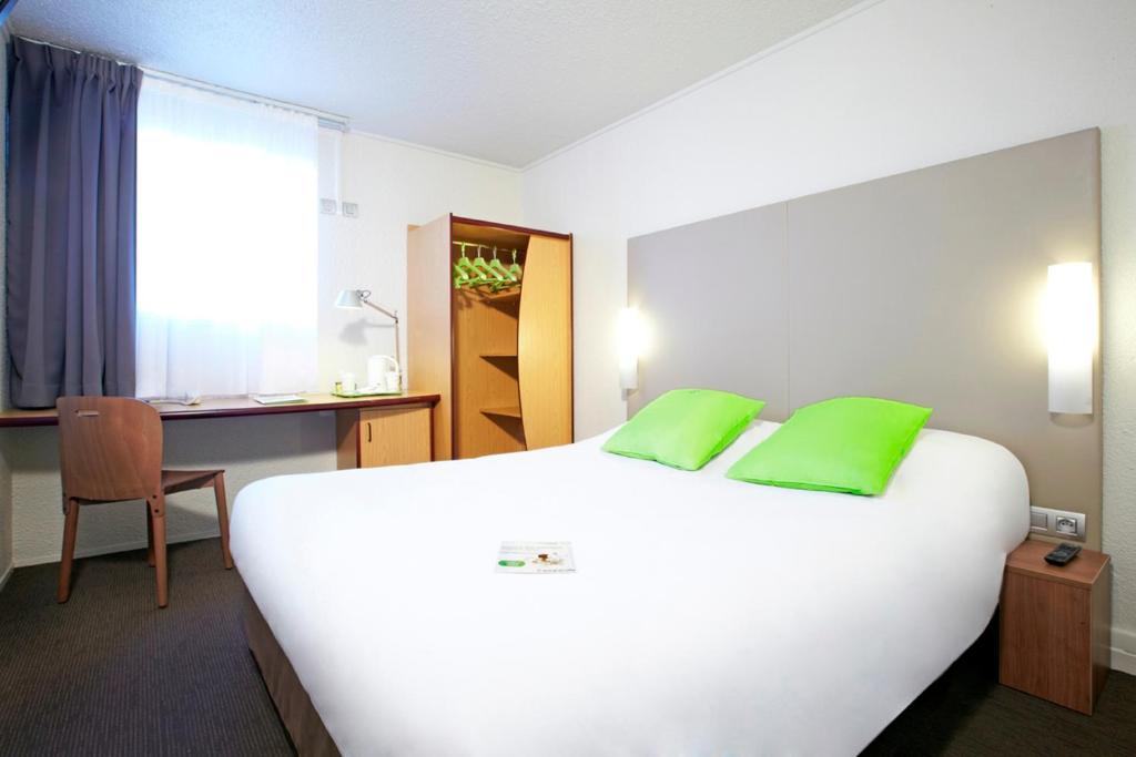 Habitación de hotel con cama blanca grande con almohadas verdes en Campanile Lyon Dardilly Porte De Lyon, en Dardilly