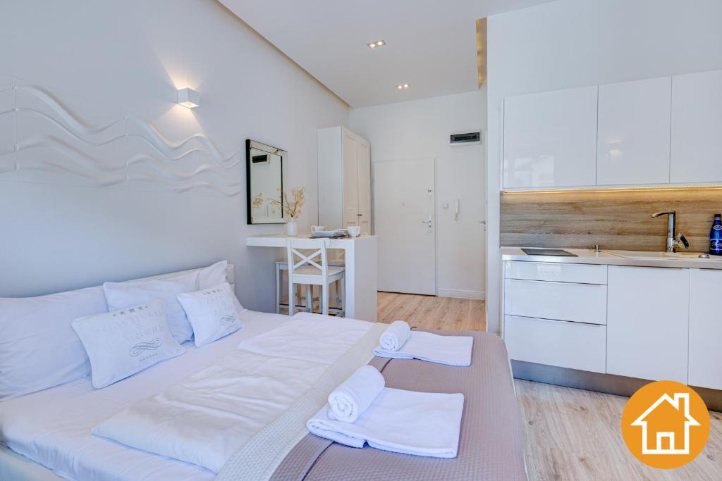 a bedroom with a large white bed and a kitchen at Apartamenty Marea - visitopl in Międzyzdroje