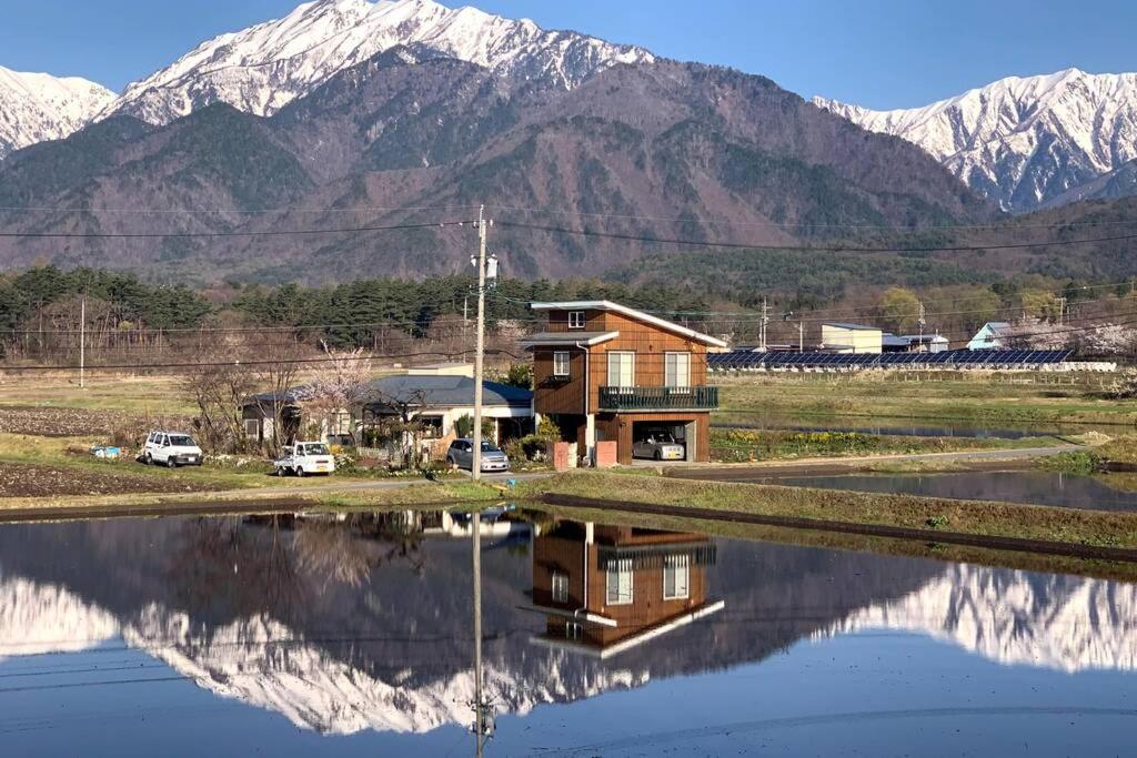 uma casa com um reflexo na água com montanhas em コテージ野の香 em Omachi