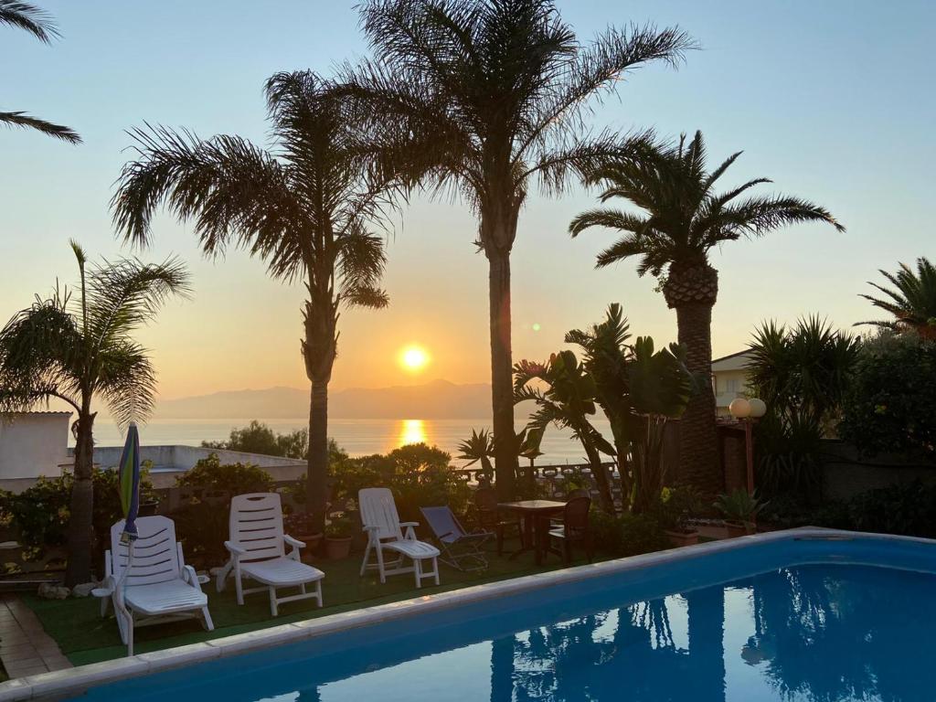a swimming pool with palm trees and a sunset at Villa Maria in Reggio di Calabria