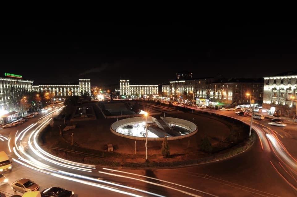 a city street at night with a fountain and buildings at Квартира около станции метро с балконами in Yerevan