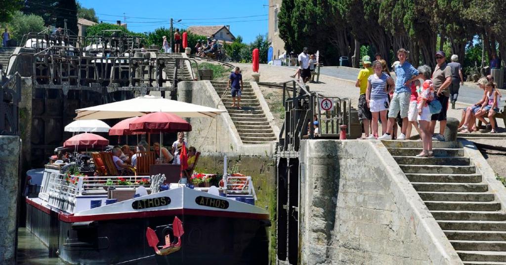 a boat in a canal with people standing on the stairs at "Le Patio"-Meublé de Tourisme 3 étoiles -Résidence "Les Logis de Béziers"-Garage optionnel-Cœur de ville-Plages à 16km ! in Béziers