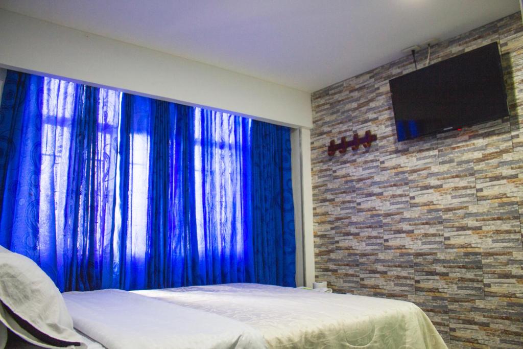 a bedroom with blue curtains and a tv on a brick wall at Hotel Punto 100 in Bogotá