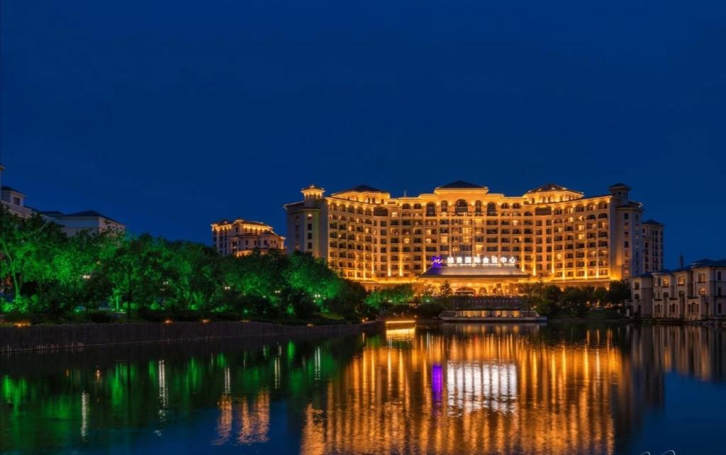 Grand Metropark Longxi Conference Center Beijing في بكين: فندق بالليل وانعكاسه في الماء