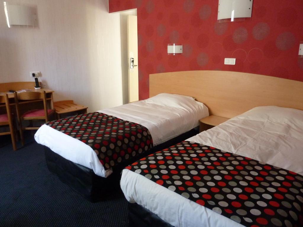 Cette chambre comprend 2 lits et une table. dans l'établissement Cit'Hotel de La Vallée, à Lourdes