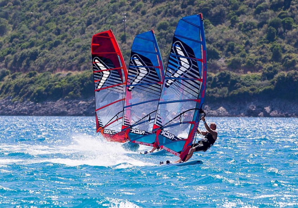 a man windsurfing on the water with three sailboats at Ammos & Thalassa in Vasiliki