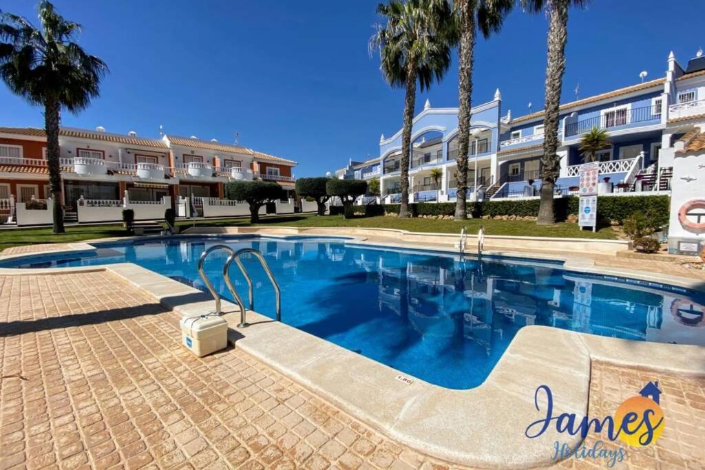 a swimming pool in front of a building with palm trees at Laguna Townhouse overlooking Communal Pool LOM01 in Ciudad Quesada