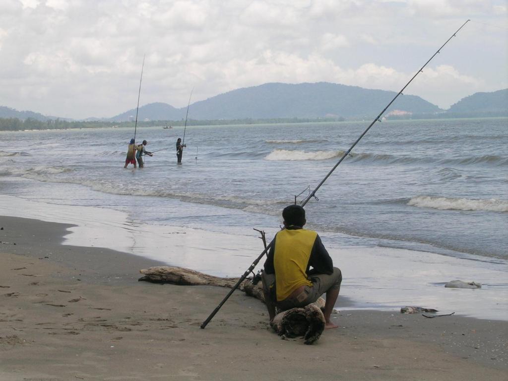 a man sitting on the beach holding a fishing pole at Cempaka Beach Resort in Kuantan
