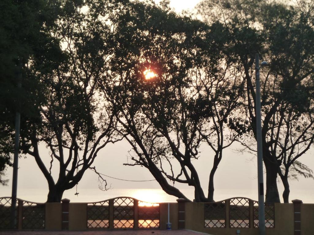 a sunset behind some trees with a fence at Cempaka Beach Resort in Kuantan