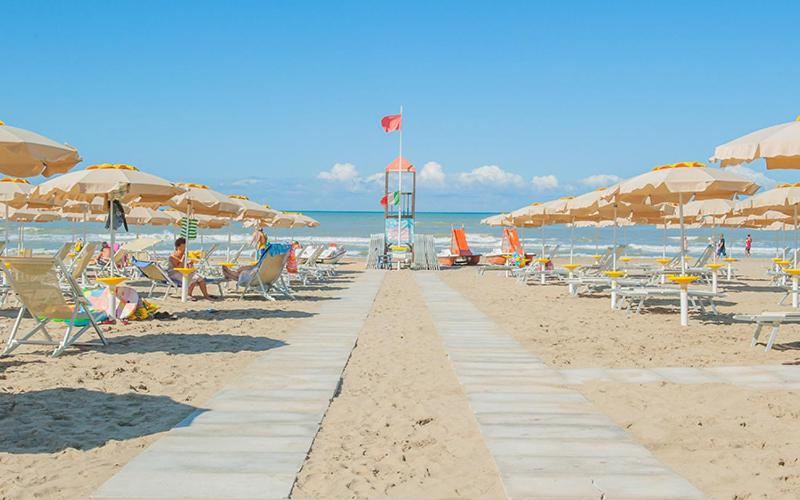 una playa de arena con sillas y sombrillas y el océano en Residence Stabilimento Roma, en LʼAmericano