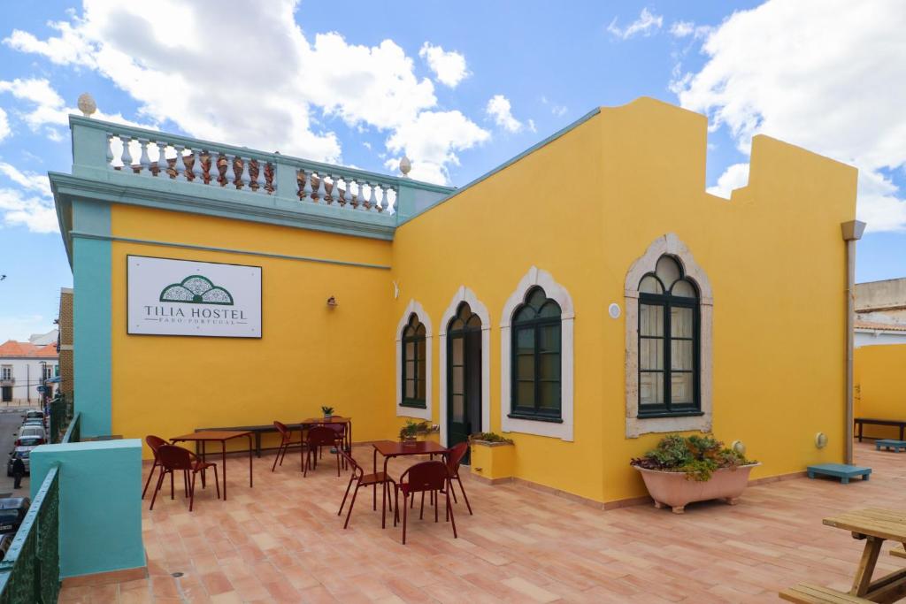 a yellow building with tables and chairs on a patio at Tilia Hostel in Faro