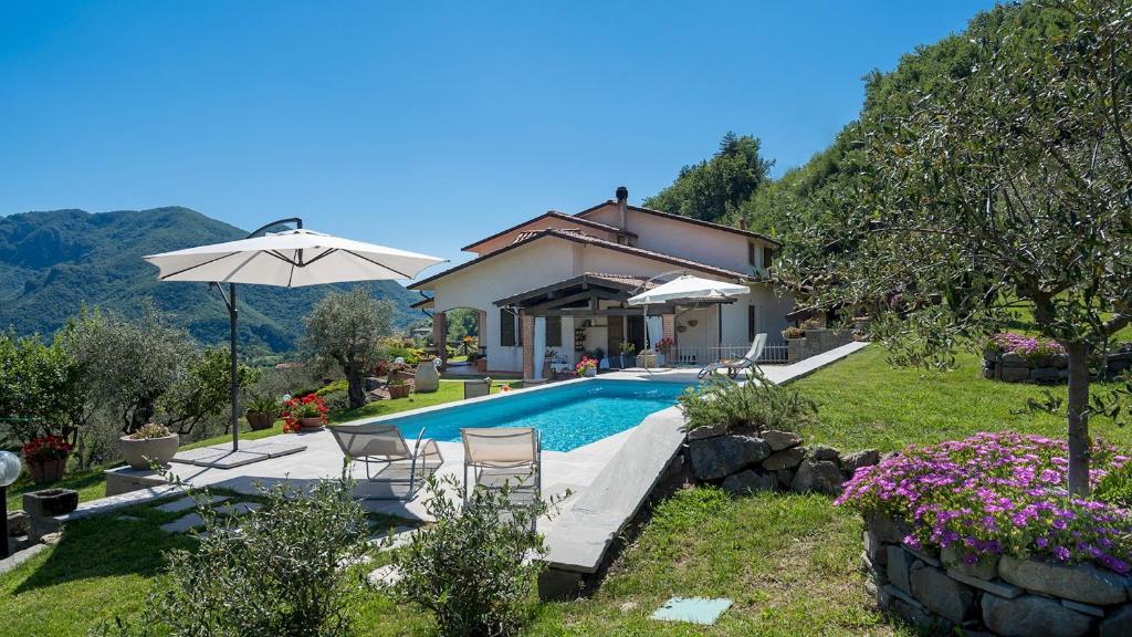 una piscina con sillas y una sombrilla junto a una casa en VILLA COSTANZA 6, Emma Villas, en Fivizzano