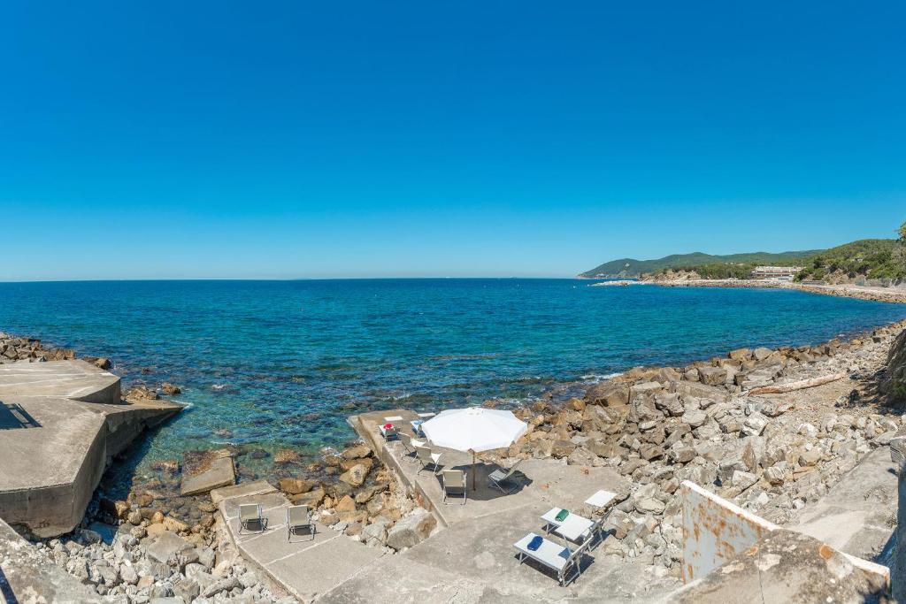 uma praia com um guarda-sol branco e cadeiras e o oceano em Villa Dell'Angelo 10, Emma Villas em Rosignano Marittimo
