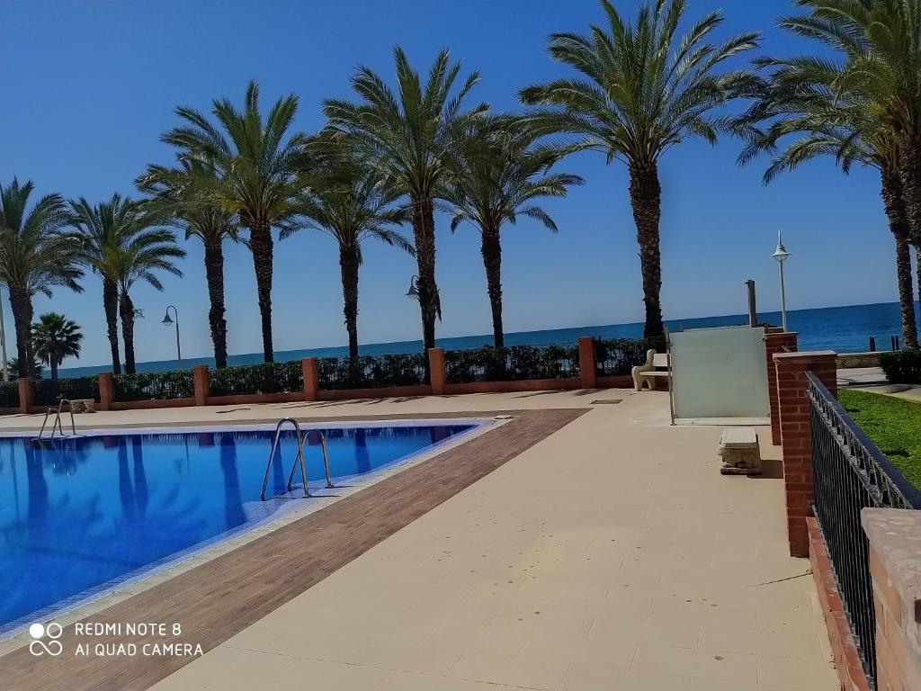 uma piscina com palmeiras e o oceano em BEACHFRONT APARTMENT in Algarrobo Costa (La Axarquía), next to Torre del Mar em Algarrobo
