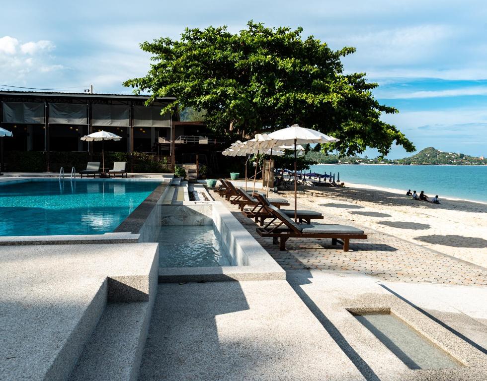 a swimming pool with benches and umbrellas on a beach at The Hive Hotel in Lamai