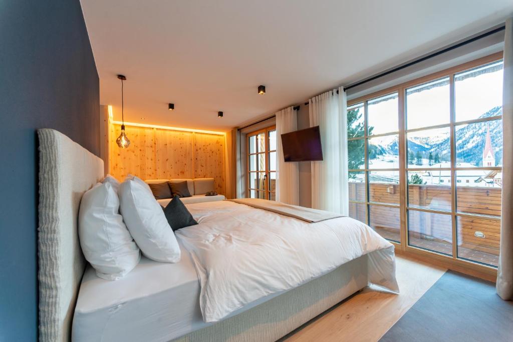 Schlafzimmer mit einem weißen Bett und einem großen Fenster in der Unterkunft Penserhof - Alpine Hotel & Restaurant in Sarntal