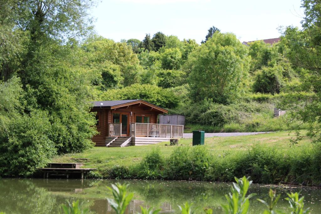 a cabin in the woods next to a body of water at Viaduct Fishery Holiday Lodges in Somerton