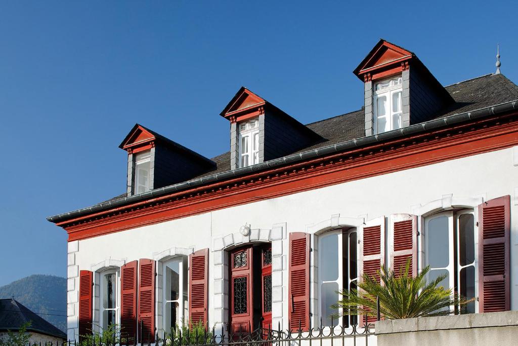 um edifício branco com persianas vermelhas e um telhado em Gaïnaa em Arudy