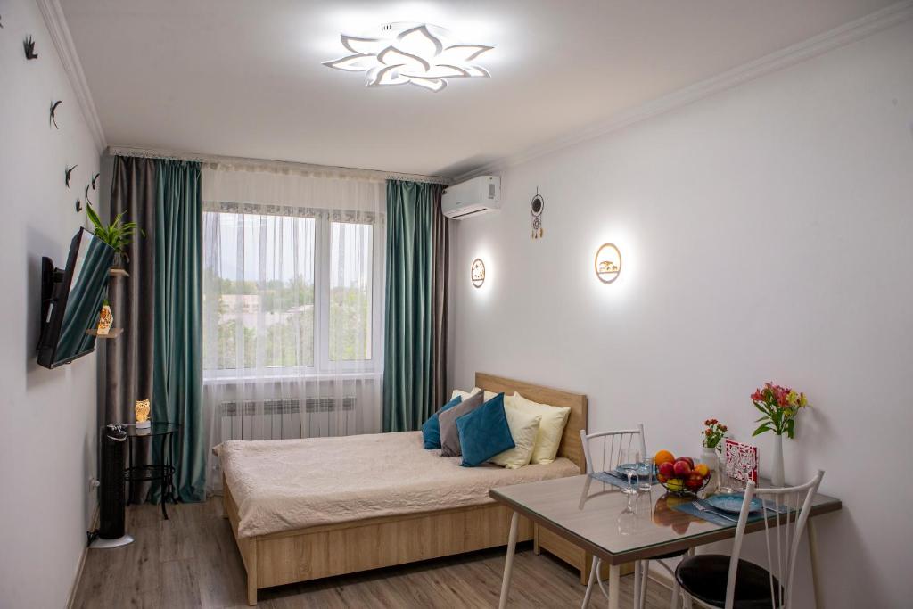 um quarto com uma cama, uma mesa e uma janela em Уютная студия с видом на горы em Almaty