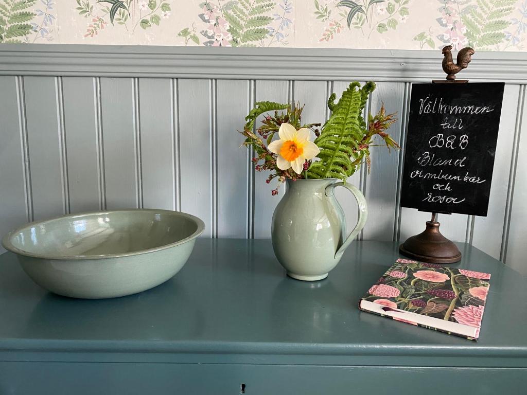 una mesa con un tazón y un jarrón de flores y una señal en B&B Bland ormbunkar och rosor, en Falkenberg