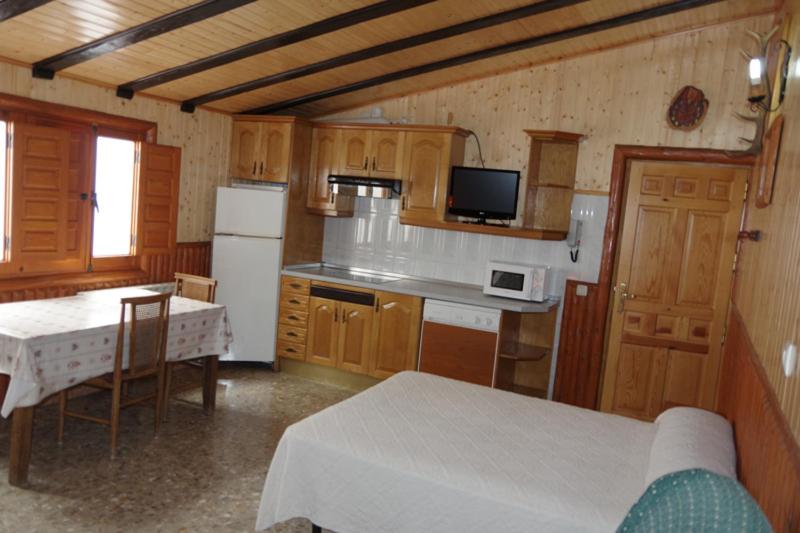 cocina con armarios de madera, mesa y nevera en CASA RURAL JAVIER " ESTUDIO"e, en Las Majadas